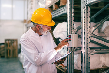 Senior worker in work wear using tablet and checking temperature in warehouse.