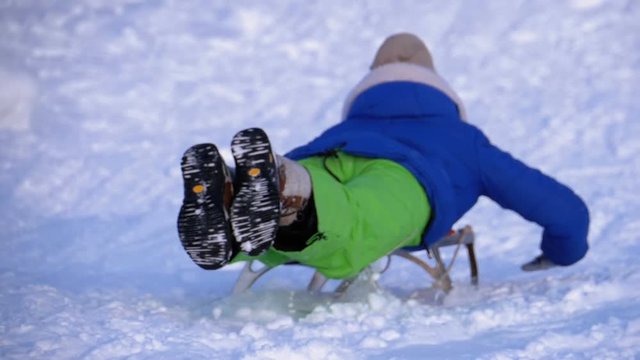 Children Sledding Down a Snowy Hill. Slow Motion in 180 fps. Happy kids move down on a sled. Fun winter holidays. Teenagers children leading down hills, sleigh ride through snow. The descent on a