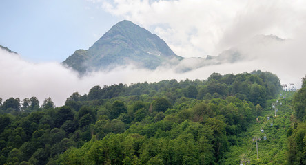 Panoramic view of green mountains with cable car and peaks in dense fog