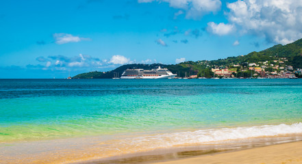 Tropical beach with in the background a luxury cruise ship in the harbor.