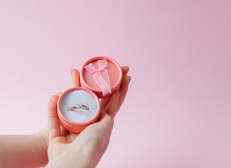 Woman opens a gift box with jewellery. Wedding ring in a box in the hands of women on a pink...