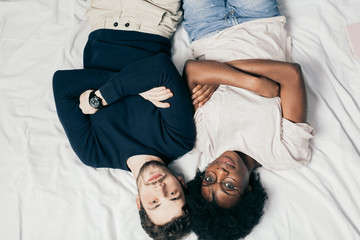 Mixed race couple of young european guy and african girl lying together in bed, relaxing together in their first vacation day, top view.