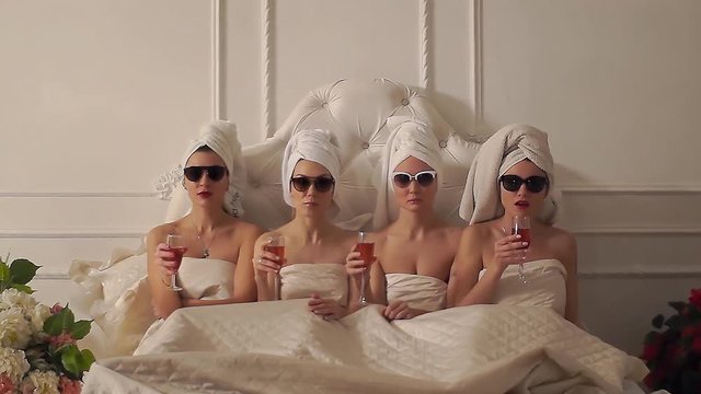 four girls in towels lie in bed and stare fixedly at the camera. girlfriends spend time together. girls at a bachelorette party in the spa