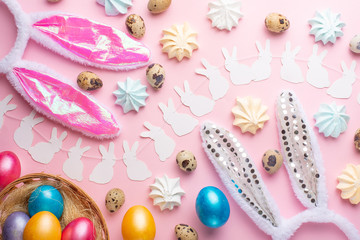 Easter holiday background. Easter eggs colored with rabbit ears on a pink background with sweets. Flat lay, horizontal composition. Greeting card concept
