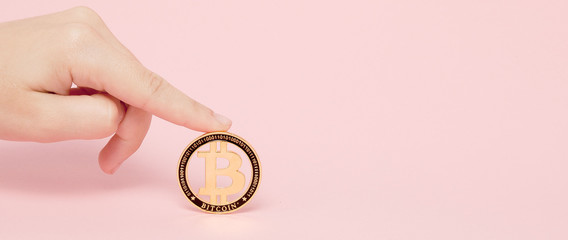 Woman is hand holding glowing new gold bitcoin on a pink background, copy space for text
