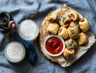 Served appetizers table - minced puff pastry rolls and beer on grey background, top view. Flat lay....