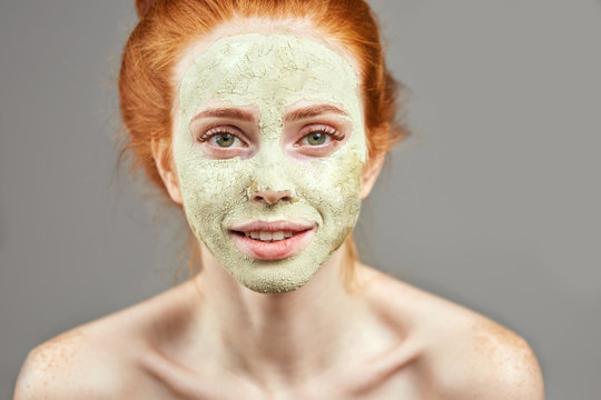 awesome ginger smiling girl is waiting for drying her mask. close up photo. studio shot