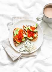 Delicious breakfast or snack - red caviar, avocado sandwiches and blue cheese on light background, top view