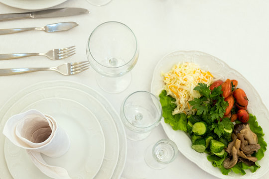 Sauerkraut, mushrooms, tomatoes, cucumbers, lettuce. Dish from the menu with cold snacks. Plates, napkins, forks, knives, glass goblets. Table setting in a restaurant.
