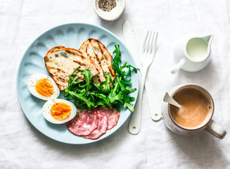 Delicious breakfast or snack - salami sausage, boiled egg, arugula, grilled bread and coffee on a light background, top view