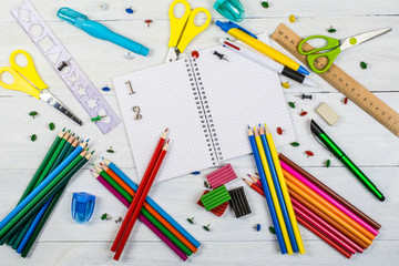 School supplies and an open notebook lie on a white wooden background.