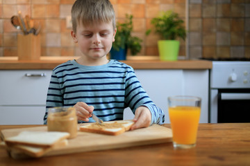 Obraz na płótnie Canvas Boy making a sandwich with peanut butter on the kitchen