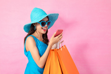 Portrait of a happy Asian pretty girl holding shopping blue bags away isolated over pink background,colorful shopping concept.