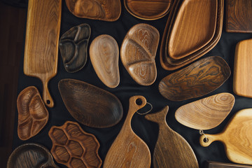 Top view of unused brand new brown handmade wooden kitchen utensil, made from different wood species, dish plate and cutting board on black background