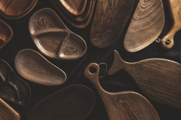 Top view of unused brand new brown handmade wooden kitchen utensil, made from different wood species, dish plate and cutting board on black background