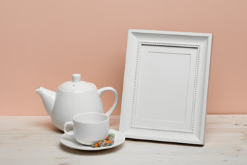 white frame with cup and teapot on white desk near pink wall