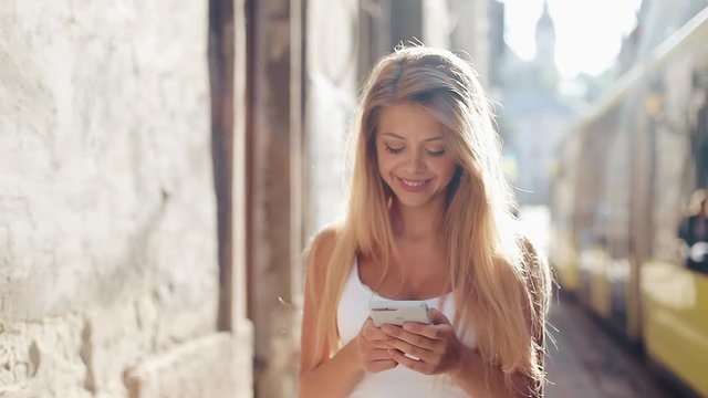 Young woman using smartphone walking in the beautiful European city. Slow Motion. Girl browsing Internet, searching for maps and information, communicating. Travel