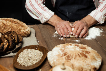 Male Chef kneads the dough with both hands until it becomes elastic, cooking delicious pizza or pastry over studio dark background.