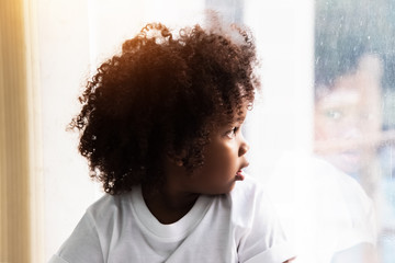 The little girl with curl hair looking outside window,doubt feeling,blurry light around