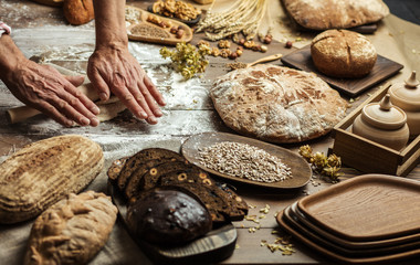 Baker prepares bread, rolls the dough with a wooden rolling pin. Kitchen old wooden table with assortment of baked goods. Top view.