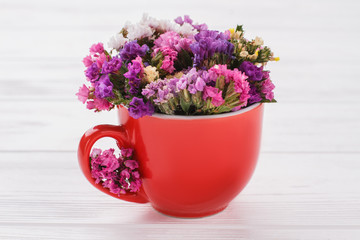 Colorful statice limonium flowers in coffee cup. White wooden table background.