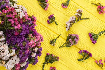 Limonium statice flowers scattered around. Top view. Yellow wood background.