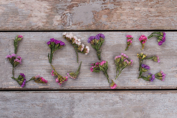 Love word made of statice limonium flowers. Top view. Old vintage wooden desk surface background.