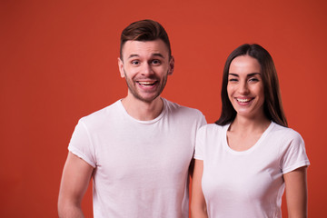 Obraz premium Happy and excited couple are posing in white t-shirts on orange background