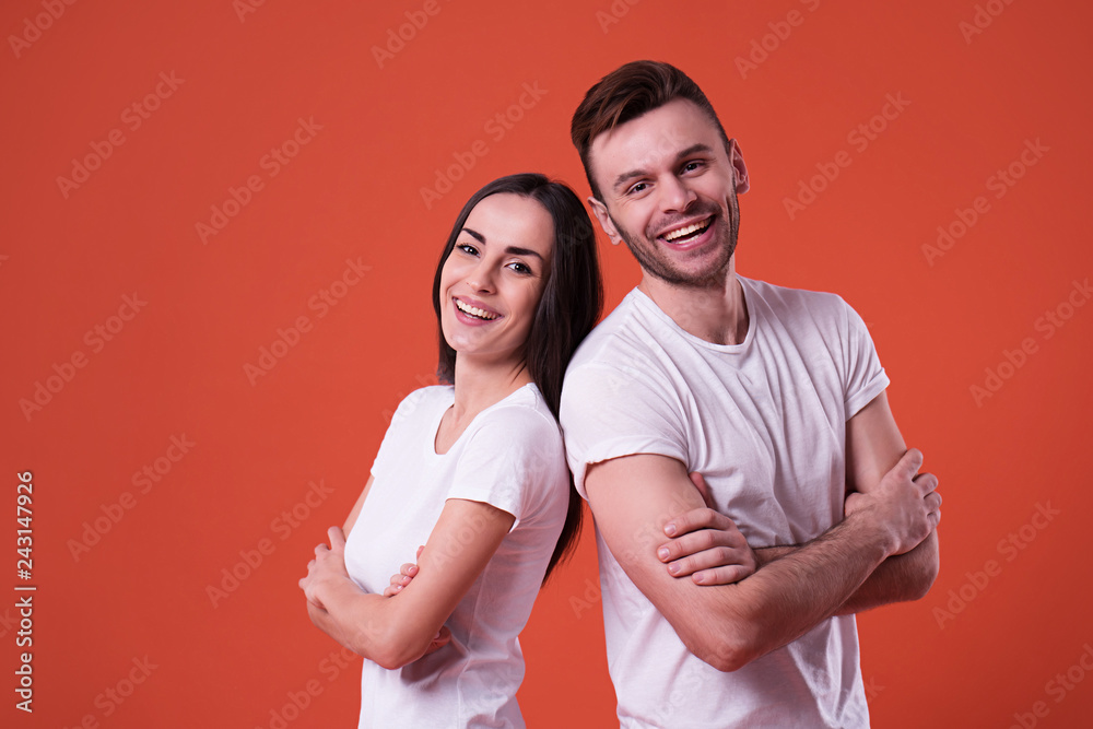 Wall mural Happy and excited couple are posing in white t-shirts on orange background