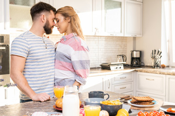 Side view portrait of loving young couple embracing in kitchen while cooking breakfast together , copy space