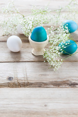 Delicate spring white flowers and painted Easter eggs on a wooden tabletop. One egg in the stand. Empty space for text