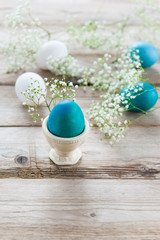 Delicate spring white flowers and painted Easter eggs on a wooden tabletop. One egg in the stand. Space for text