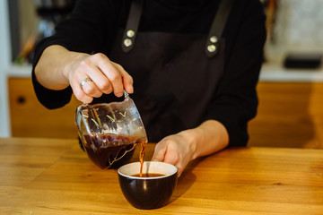 Close up of female barista's hands pouring coffee into cup on bar counter in cafe