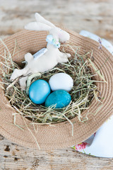Rustic wicker hat with bright Easter eggs and textile rabbit on wooden floor