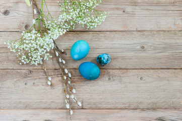 Light wooden background and bright blue Easter eggs with spring flowers. Place for text