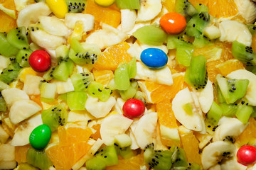 Sweet fruit dessert. On a plate, chopped bananas, oranges, apples, kiwi, poured with condensed milk.