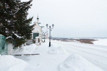 Winter landscape: embankment of the river Sukhona in Veliky Ustyug in the snow in winter: dome of the church, lights and drifts