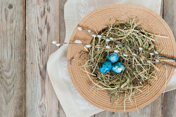 Nest in a wicker hat and painted spotted Easter eggs with spring flower. Flat lay