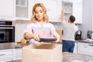 Waist up portrait of young housewife unpacking boxes with new tableware and plates after moving house, copy space