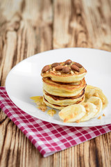 Pancakes with banana,nuts and honey on white plate for breakfast on wooden background with copy space.