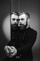 Black and white photo of a man with a beard and stylish hairdo dressed in the black shirt standing...