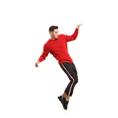 Young stylish man dressed in red turtleneck and dark pants with stripes on the sides dances on the white background in the studio