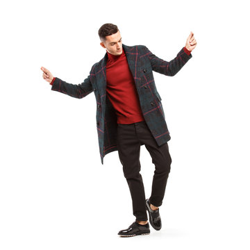 Young Stylish Man Dressed In Red Turtleneck, Brown Pants And A Plaid Coat Poses On The White Background