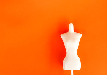 White plastic female mannequin figure on bright orange background