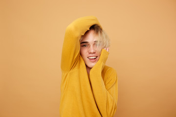 Blond guy dressed in yellow sweater is posing  with his hands on his face on the beige background...