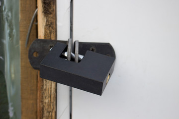 Closed new grey metal padlock close-up hangs on old white door. Background symbolizing closed or denied entry