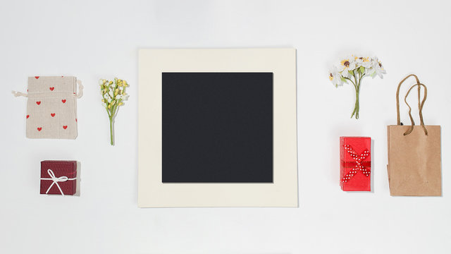 Composition with black photo frame, red gift boxes, craft bag, canvas bag with red heart shapes and spring field flower on white table. Flat lay mockup for bloggers, designers, photographers, etc