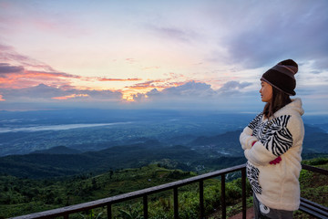 Fototapeta na wymiar Woman tourist in a sweater dress watching the beautiful nature landscape of the forest and mountain during the sunrise on the high peak in the morning at Phu Thap Boek Viewpoint Phetchabun, Thailand