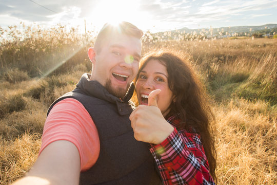 Travel, tourism and nature concept - Smiling couple taking selfie on field and showing thumbs up