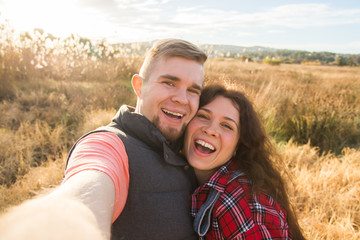 Travel, vacation and holiday concept - Happy couple having fun taking selfie against background on the field